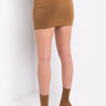 A person stands against a white background, facing away from the camera. They are wearing a caramel-colored RIDE WITH ME UTILITY MINI SKIRT and matching ankle-high heeled boots. The skirt features pocket details and belt loops at the waist.