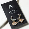 The SEE THE REAL ME RHINESTONE EARRING SET from AKIRA Accessories comes displayed on a sleek black cardboard holder. This set includes two pairs of gold-toned earrings featuring intricate designs with sparkling clear rhinestones in leafy and floral shapes, perfect for any occasion: one pair of studs and one pair of drop earrings.