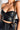 A person wearing the Moto Dreamer Pleather Bandeau Top featuring black faux leather, gold zippers, and buttons, paired with black high-waisted pants. They are carrying a black handbag with a gold chain strap. The image focuses on the upper torso and accessories, set against a white background.