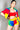 A woman is posing against a plain background wearing a colorful outfit. She has a confident expression and is dressed in a red sports bra and the NUMBER ONE FAN FULL ZIP SHORT SLEEVE JACKET paired with matching shorts in red, yellow, blue, and green blocks.