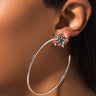 Close-up of a person wearing the STAR LIGHT HOOP earring. The earring features a large silver hoop with a star-shaped stud at the top, adorned with small black stones. The person's ear and part of their dark hair and neck are visible.