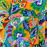 A close-up of the vibrant, colorful fabric of the TAKE ME TO THE TROPICS MAXI SKIRT, featuring a kaleidoscopic floral design with intricate patterns in bright shades of blue, pink, green, and purple on a bold orange background, gathered or pleated in sections.