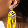 Close-up of a person wearing the TALK TO THE HAND FRINGE EARRING. The earring showcases a glittering stud at the top, attached to an eye-shaped design adorned with sparkling details and yellow bead fringes hanging below. The earring stands out against the person's smooth skin.