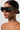 A woman with smooth, dark skin and a sleek, low bun wears large TELL ME NOTHING RHINESTONE SUNGLASSES ASSORTED. She has gold hoop earrings and multiple small piercings along her ear, set against a plain, light-colored background.