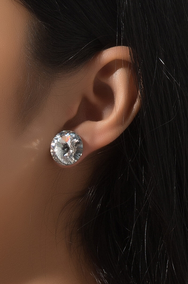 Close-up of a person's ear adorned with a TINY DANCER STUD EARRING. The lighting accentuates the sparkle of the crystal while the individual's dark hair partly frames the ear.