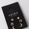 A set of gold-toned earrings attached to a black card labeled "AKIRA Accessories," named the "TO THE MOON STUD PACK." The set includes star-shaped earrings with a small gem in the center, studded bows, and crescent moon-shaped earrings with small clear stones. The background is plain light gray.