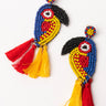 Introducing the TOUCAN SAM EARRING: This vibrant pair of beaded earrings showcases intricate patterns in the shape of toucans. Featuring a stunning array of beads in black, yellow, blue, and red, each earring is adorned with dangling red and yellow tassels. The design is completed with a beaded backing for the ear stud.