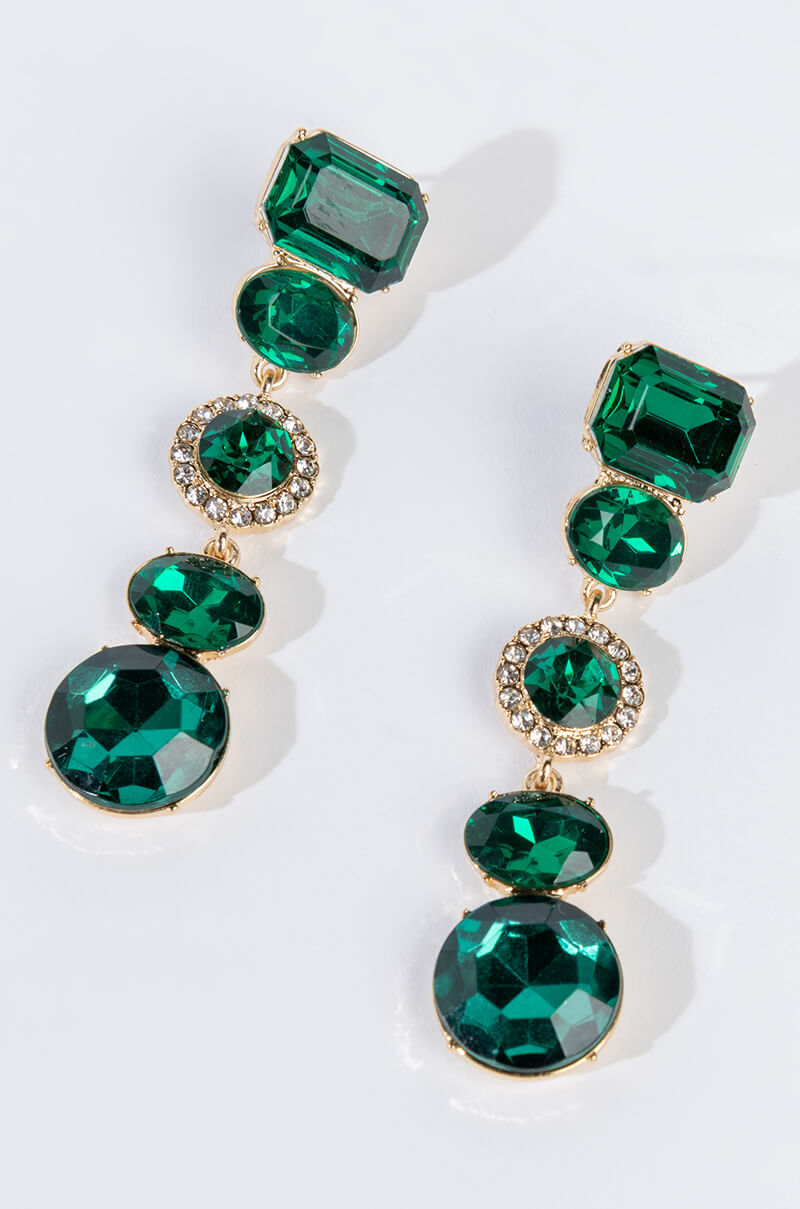 Introducing the VENUS GODDESS EMERALD DROP EARRINGS: a striking pair adorned with multiple emerald-green gemstones in an array of shapes, bordered by delicate clear crystals. The gemstones are set in a gold-tone metal, offering a luxurious and elegant aesthetic.