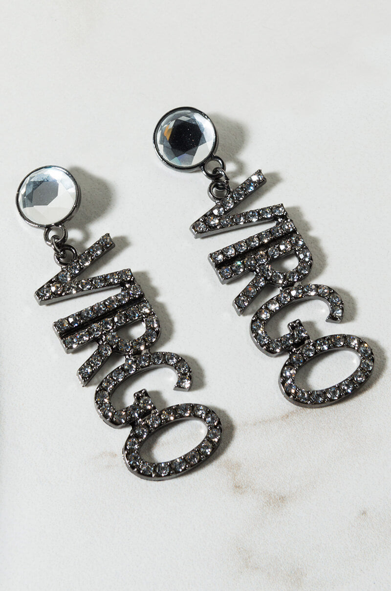 The Virgo Rhinestone Earrings are showcased on a light surface. Each earring showcases a large, round, faceted gem at the top with the word "Virgo" dangling below, adorned with small, sparkling rhinestones.
