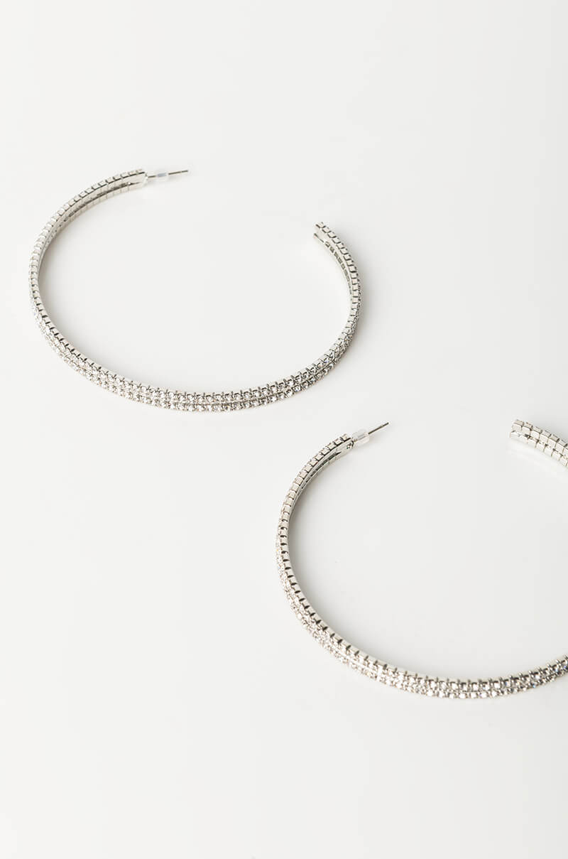 A pair of WAP BLING HOOP EARRINGS is displayed on a white background. These sparkling silver hoop earrings are adorned with small, shiny rhinestones, giving them a glittering appearance. They have a semi-circular shape and a slender design, perfect for an elegant look.