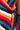 A close-up image of the SEXY MULTI COLOR STRIPE DRESSY MINI, showcasing its vibrant vertical bands of red, orange, yellow, white, dark blue, and teal. The dress is elegantly tied with a matching fabric belt on the side. A person's hand with pink nail polish is partially visible on the left.