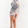 A woman with long dark hair in a ponytail stands against a plain white background. She is wearing the WELCOME TO MY LAIR LONG SLEEVE SHEER MINI DRESS, which features a fitted, high-neck design with a swirling gray and white marble pattern. She completes her look with transparent high-heeled shoes and poses with one hand by her side.