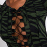 A person models the "WILD THING LACE FRONT HACCI TOP", showcasing its green and black zebra pattern. The top features black stitching along the edges and sleeves, with a deep V-neck tied with black strings for an edgy and stylish look. The background is plain white.